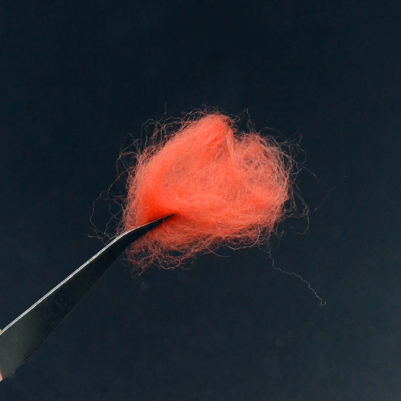 Un par de pinzas sostienen delicadamente una fibra naranja vibrante contra un fondo oscuro