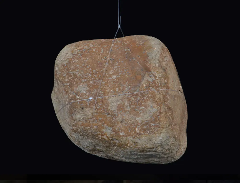 Una gran roca texturizada suspendida por cables contra un fondo oscuro