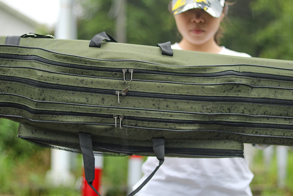Una persona que sostiene un estuche grande, verde y acolchado. El estuche parece estar diseñado para transportar o transportar equipos, posiblemente instrumentos musicales o dispositivos electrónicos, dado su acolchado protector y las correas que sugieren que se puede llevar al hombro.