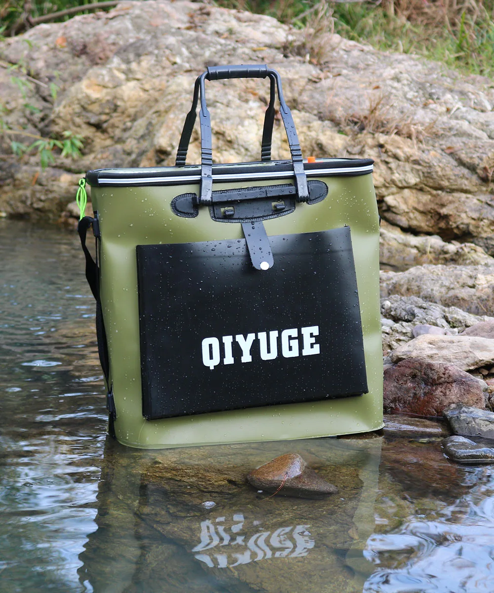 Una hielera verde y negra con tapa negra. La hielera se coloca sobre una superficie rocosa cerca de una masa de agua, posiblemente un río o un arroyo, como lo indican el borde del agua y las rocas al fondo.