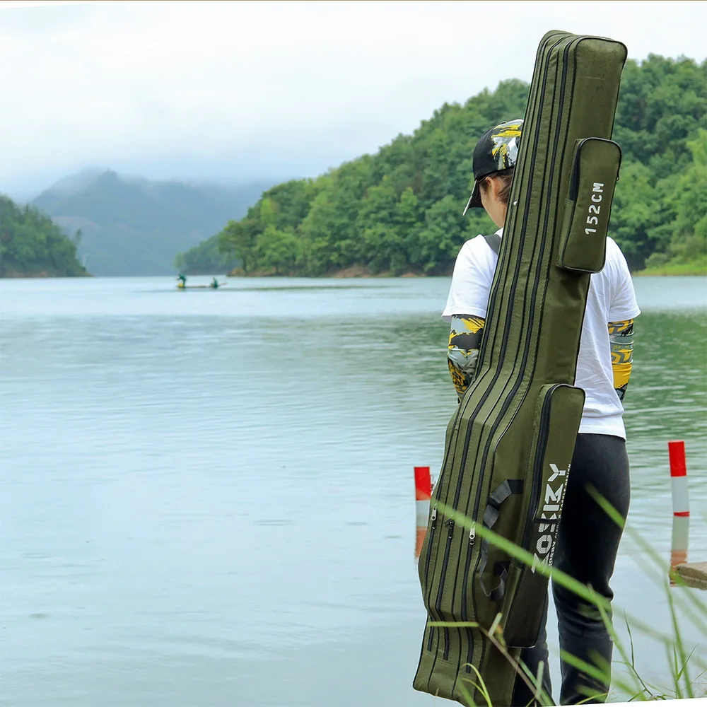 Una persona parada junto a una masa de agua, posiblemente un lago o un río tranquilo. La persona lleva una camiseta blanca y una gorra, y sostiene un estuche grande y verde que parece estar diseñado para transportar un instrumento musical, probablemente una guitarra o un instrumento de cuerda similar.