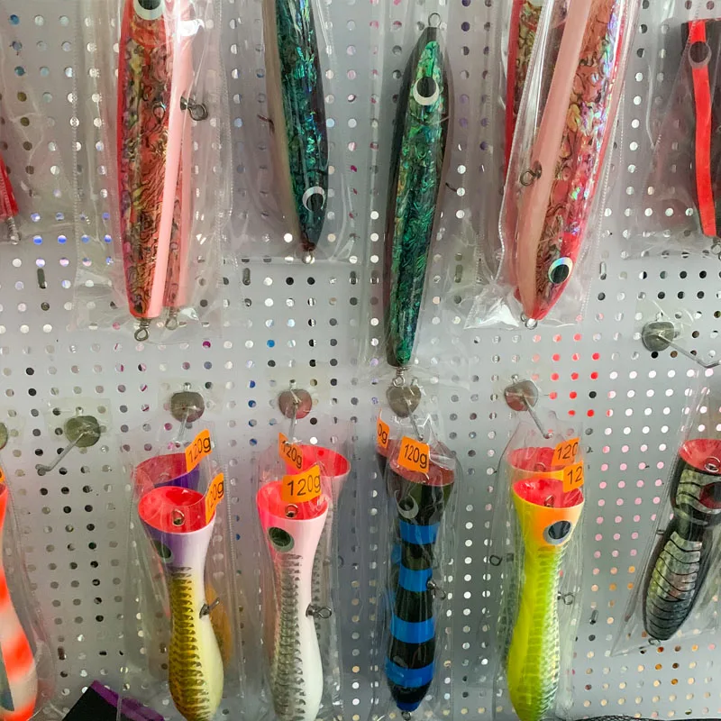 Una colección de señuelos de pesca exhibidos en un tablero perforado. Estos señuelos están diseñados para imitar la apariencia de los peces y se utilizan para atraer peces reales cuando se pesca. Vienen en varios colores, formas y tamaños para imitar diferentes tipos de peces y atraer a diferentes especies de peces.