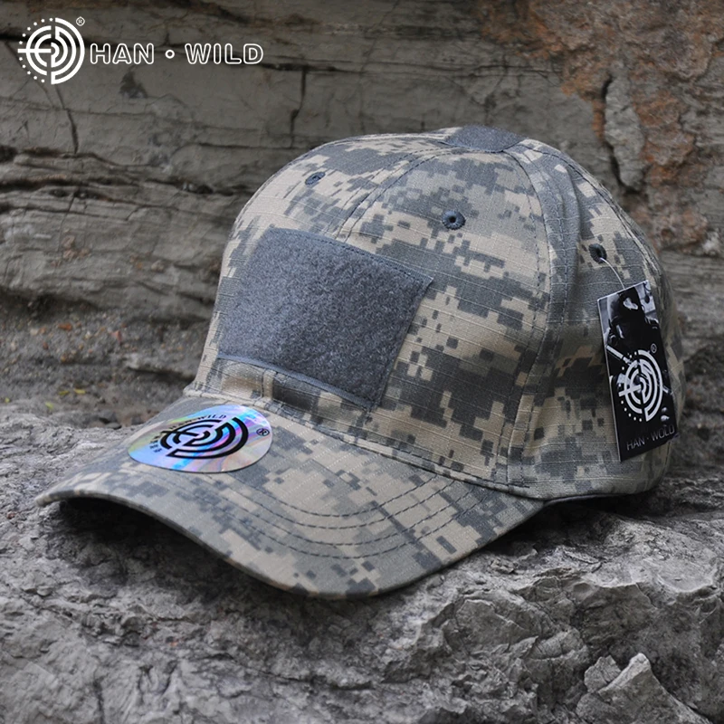 Una gorra de béisbol de camuflaje con un diseño que incluye un patrón de formas y colores que asemejan un camuflaje digital o pixelado. La gorra tiene un pequeño parche circular reflectante en la parte delantera, que probablemente esté destinado a aumentar la visibilidad en condiciones de poca luz.