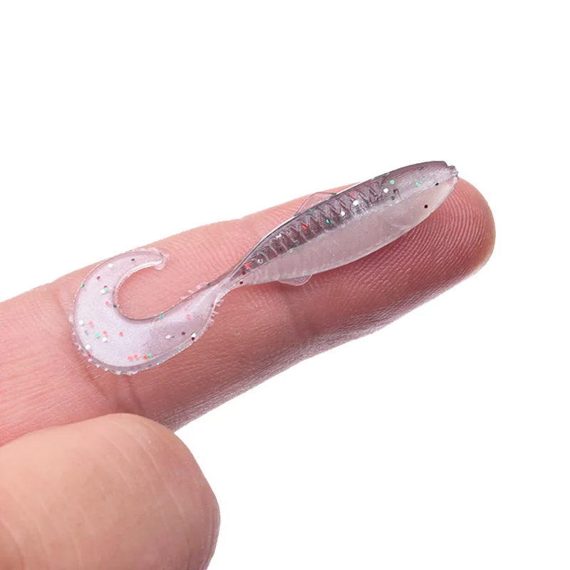 El dedo de una persona con un objeto pequeño, transparente y brillante adherido a él. El objeto parece ser un diseño decorativo de uñas, posiblemente una calcomanía para uñas o una pegatina para uñas, dado su tamaño y su textura brillante.