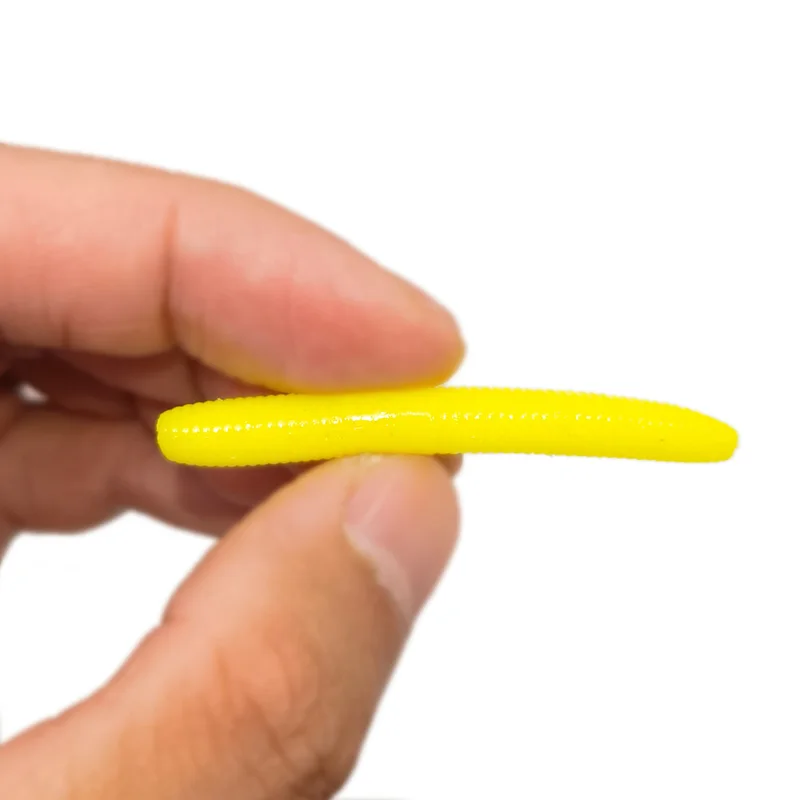 Se está sosteniendo un objeto de textura amarilla brillante que se asemeja a un gusano entre los dedos