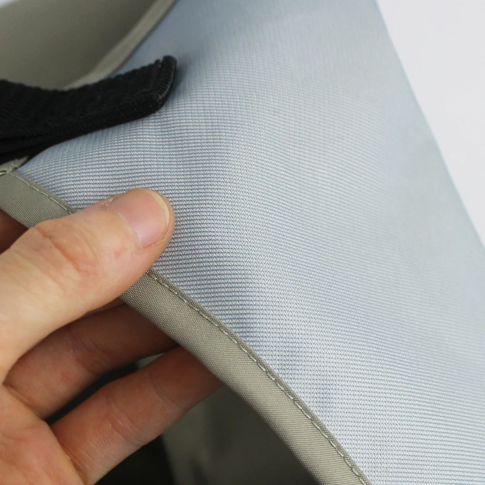 Un primer plano de la mano de una persona sosteniendo un trozo de tela o material. La tela parece ser de color gris claro o azul con un patrón texturizado, posiblemente una tela tejida o de punto.