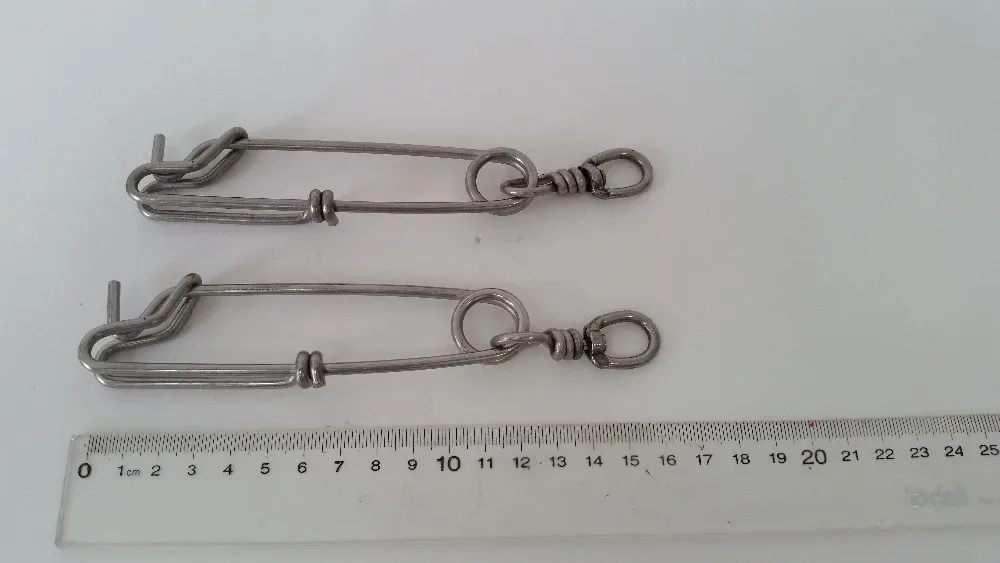 Dos mosquetones metálicos colocados sobre una superficie plana. Estos mosquetones parecen estar hechos de un metal plateado, posiblemente acero o aluminio, y tienen un mecanismo de puerta con resorte para asegurar artículos. Se colocan junto a una regla, que se utiliza para medir su tamaño.
