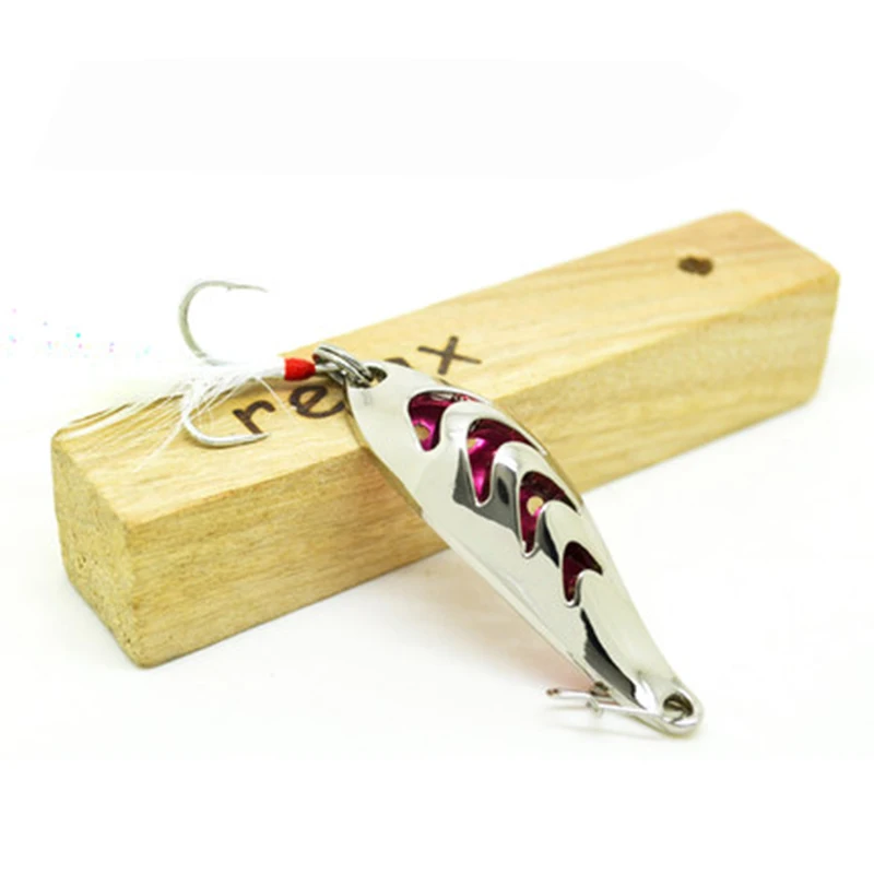 Un señuelo de pesca con un anzuelo adherido, apoyado sobre un bloque de madera. El señuelo tiene un cuerpo metálico con una combinación de colores rojo y plateado, y parece estar diseñado para parecerse a un pez o un pez cebo.