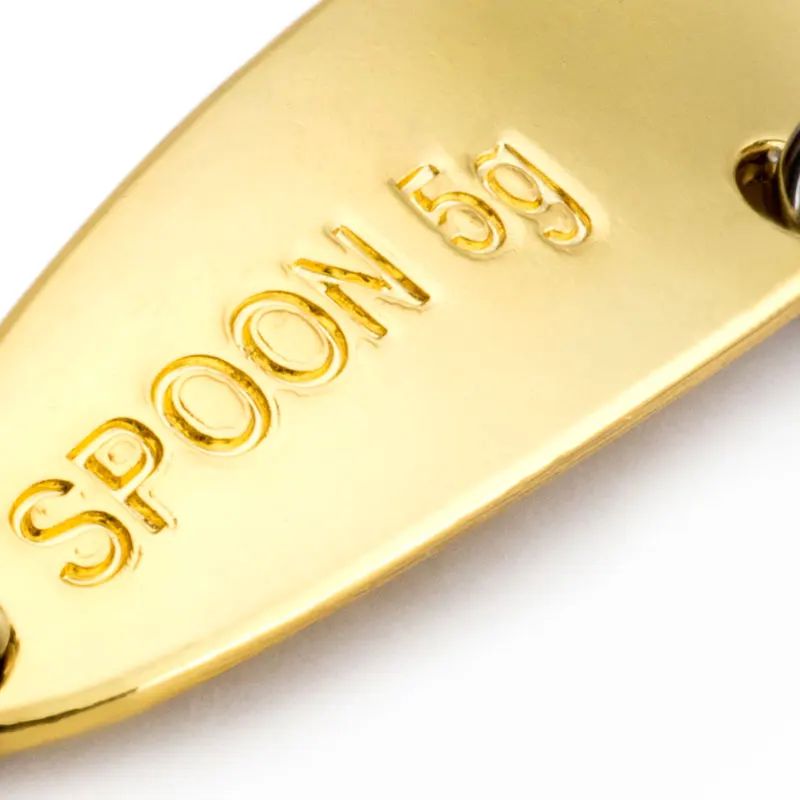 Una cuchara de color dorado con la palabra CUCHARA grabada. La cuchara parece ser un objeto decorativo o conmemorativo, posiblemente una pieza de colección o una vajilla fina.