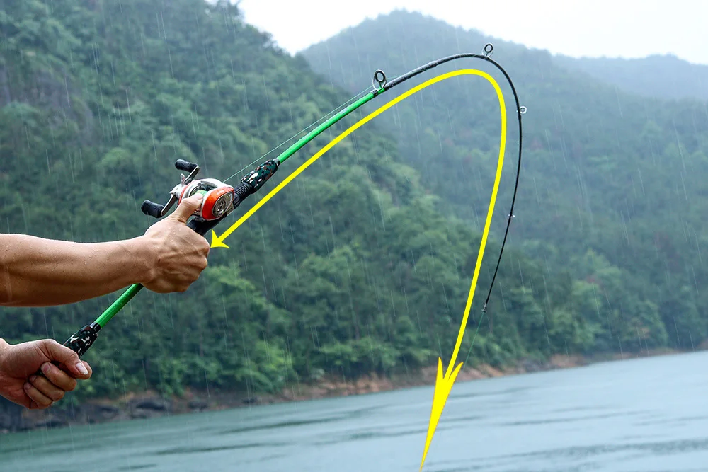 Una persona pescando en una masa de agua, probablemente un lago o río, con un paisaje montañoso de fondo. La persona sostiene una caña de pescar con una línea amarilla que se extiende hacia el agua, indicando la dirección del lance.