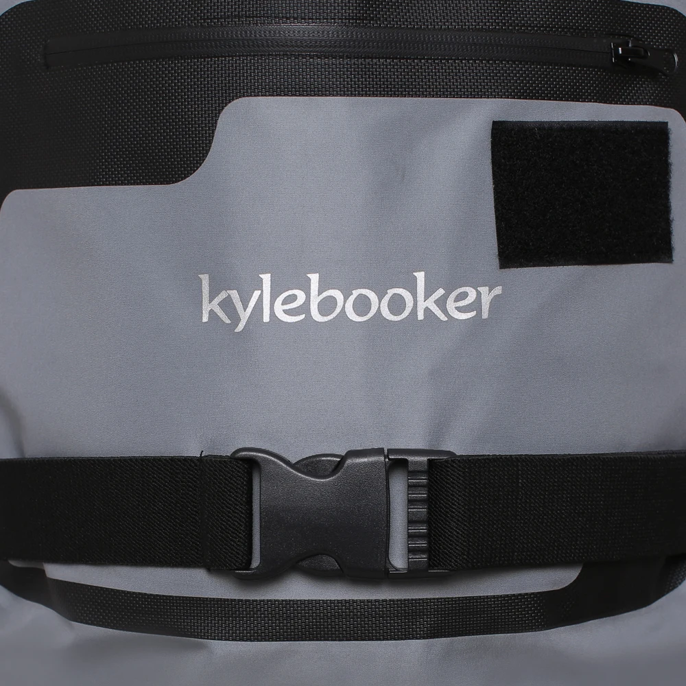 Un kytebook, que parece ser una especie de funda para portátil o funda protectora. Tiene un exterior gris con la marca kytebook impresa en blanco. Hay una correa negra con cierre de hebilla, lo que sugiere que el estuche se puede sujetar de forma segura.