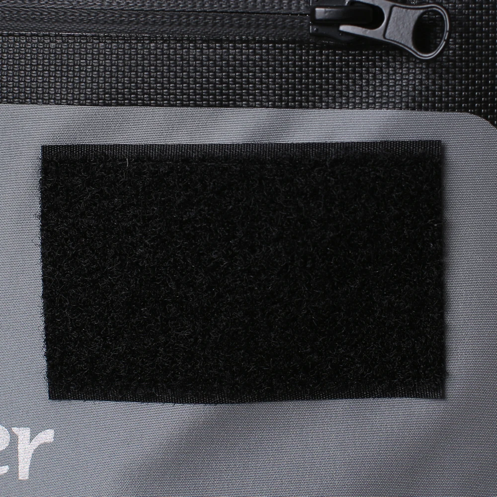 Un primer plano de una tela con una superficie texturizada, posiblemente una prenda de vestir o un material textil. Hay un tirador de cremallera visible en la esquina superior izquierda, lo que sugiere que la tela podría ser parte de una prenda con cierre de cremallera.
