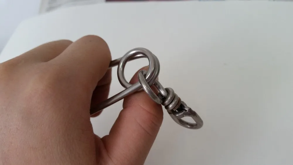 Una mano que sostiene un pequeño objeto metálico que parece ser un llavero o un llavero. El llavero tiene un lazo a través del cual se puede insertar una llave y se le adjunta una pequeña pieza de metal, posiblemente decorativa.