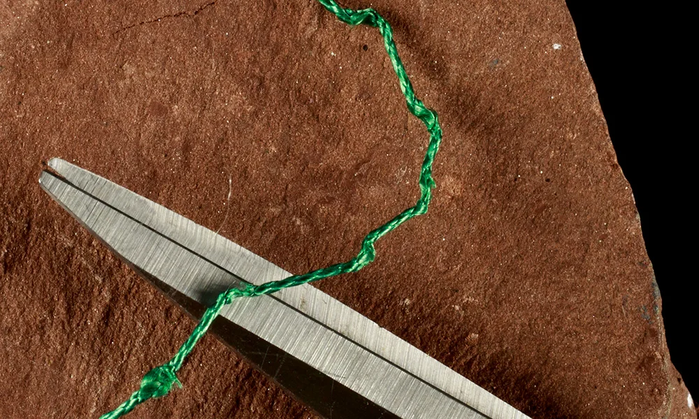 Un par de tijeras corta un hilo verde en una superficie texturizada