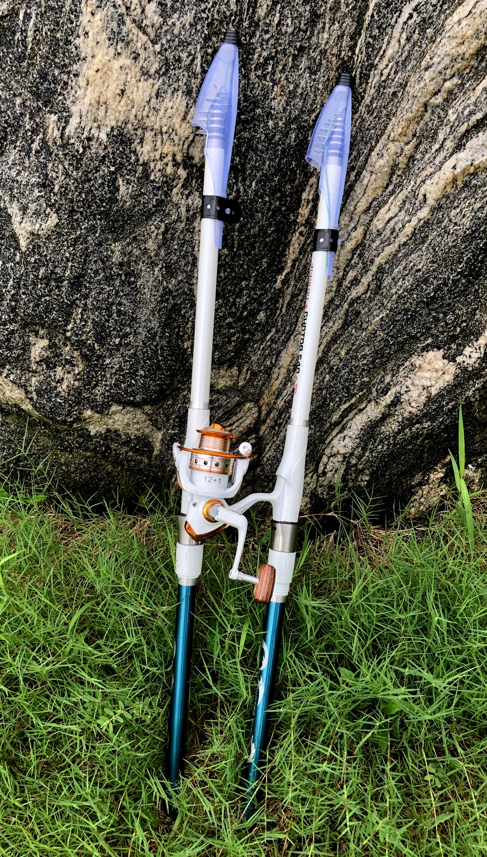Dos bastones de trekking con los mangos extendidos y las puntas introducidas en el suelo. Los bastones parecen estar hechos de un material liviano, posiblemente aluminio o fibra de carbono, y tienen un agarre de espuma para mayor comodidad.