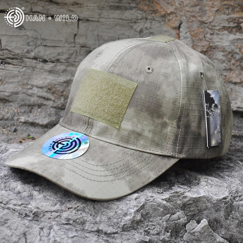 Una gorra de béisbol con estampado de camuflaje. La gorra tiene un parche en el frente, que parece ser un logotipo o emblema, y ​​hay una pequeña etiqueta adherida al ala.