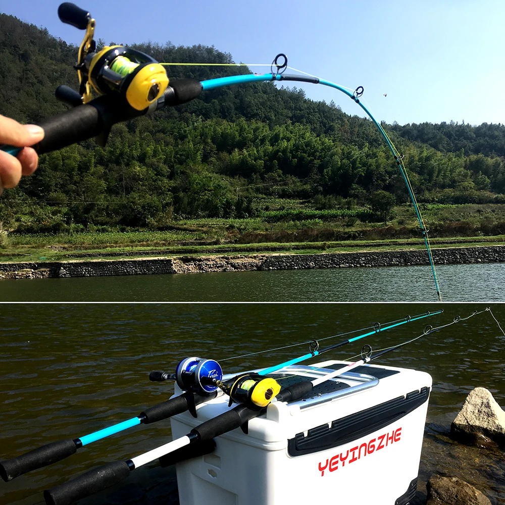 Una persona sostiene una caña de pescar con un carrete adjunto y, al fondo, hay una masa de agua, probablemente un lago o un río, con una ladera cubierta de vegetación. La caña de pescar está equipada con un señuelo, que es un tipo de cebo que se utiliza para atraer peces.