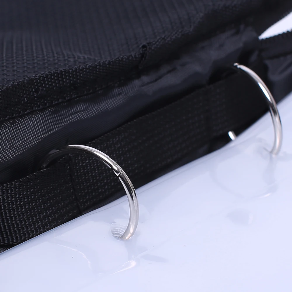 Un primer plano de una tela negra con una textura que podría ser parte de un bolso o de una prenda de vestir. Hay dos anillos de metal de color plateado adheridos a la tela, que probablemente se usan para asegurar correas o para sujetar accesorios.