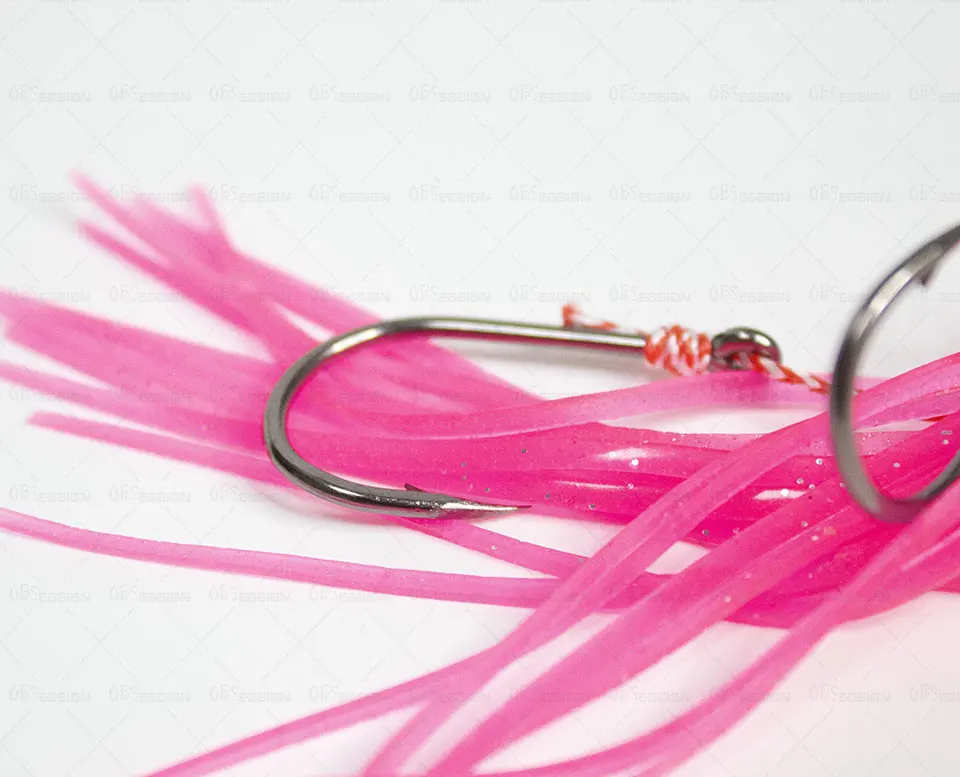 Un señuelo de pesca con cola rosa y brillante. El señuelo tiene un anzuelo de metal unido a un alambre, que probablemente se utiliza para pescar. La cola rosada está diseñada para atraer peces y el material brillante puede estar destinado a hacer que el señuelo sea más visible en el agua.