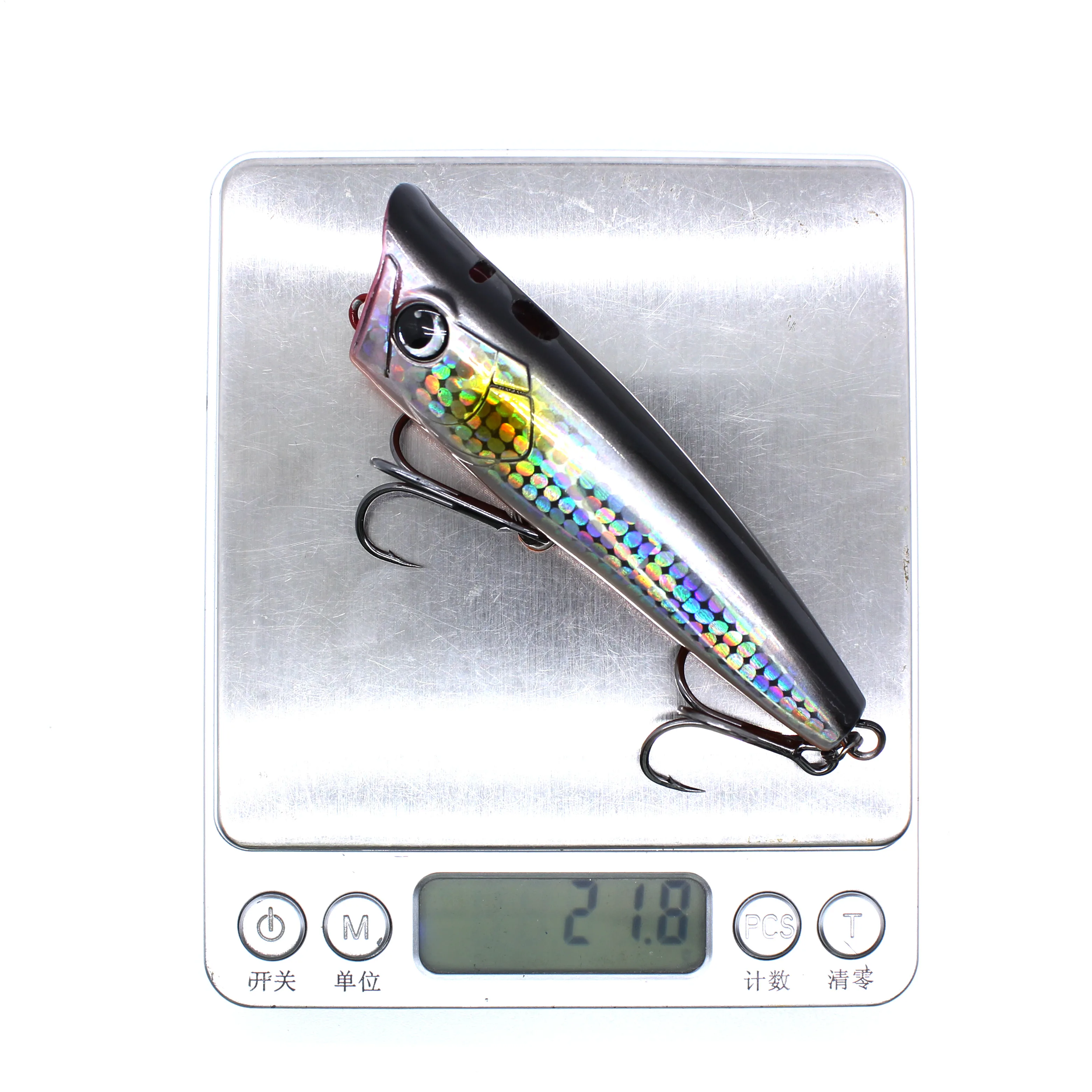 Un señuelo de pesca colorido con un patrón de escala y dos ganchos que se muestran en una escala digital