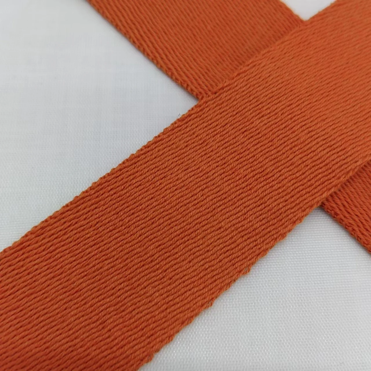 Un primer plano de una tela con textura acanalada. Parece ser una prenda de vestir o una prenda textil con patrón de punto acanalado, que se utiliza comúnmente por su elasticidad y comodidad. El color de la tela es un naranja sólido.