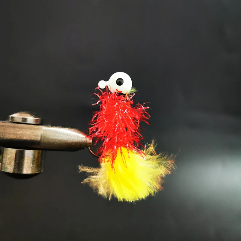 Un señuelo de pesca vibrante con un cuerpo plumoso rojo y amarillo y un gancho de ojo blanco