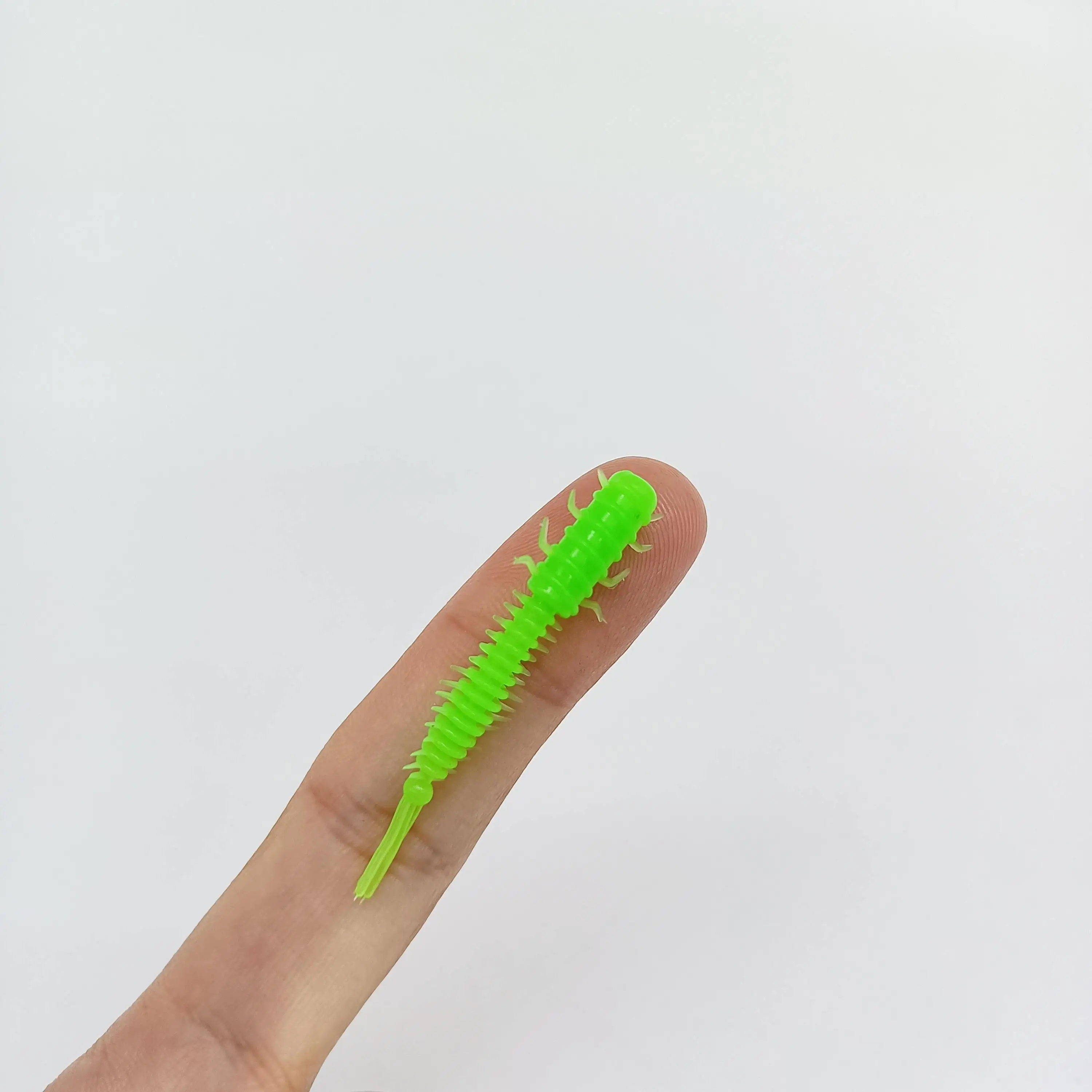 Un pequeño juguete de plástico verde vibrante que se asemeja a una oruga descansa sobre un dedo