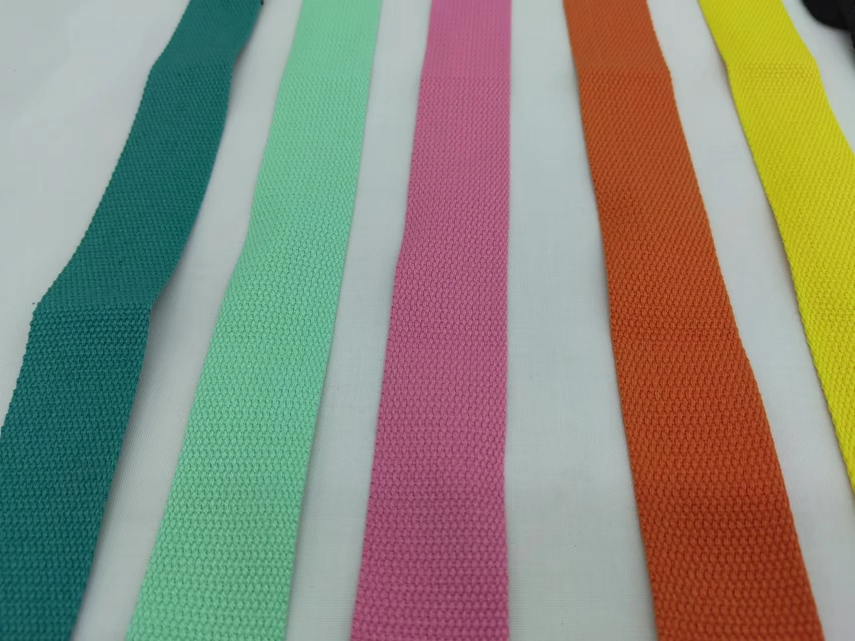 Colección de cintas o correas de tela dispuestas en fila. Vienen en varios colores: verde, rosa, naranja y amarillo. Cada cinta tiene un patrón texturizado, que puede usarse con fines decorativos o para mayor agarre.