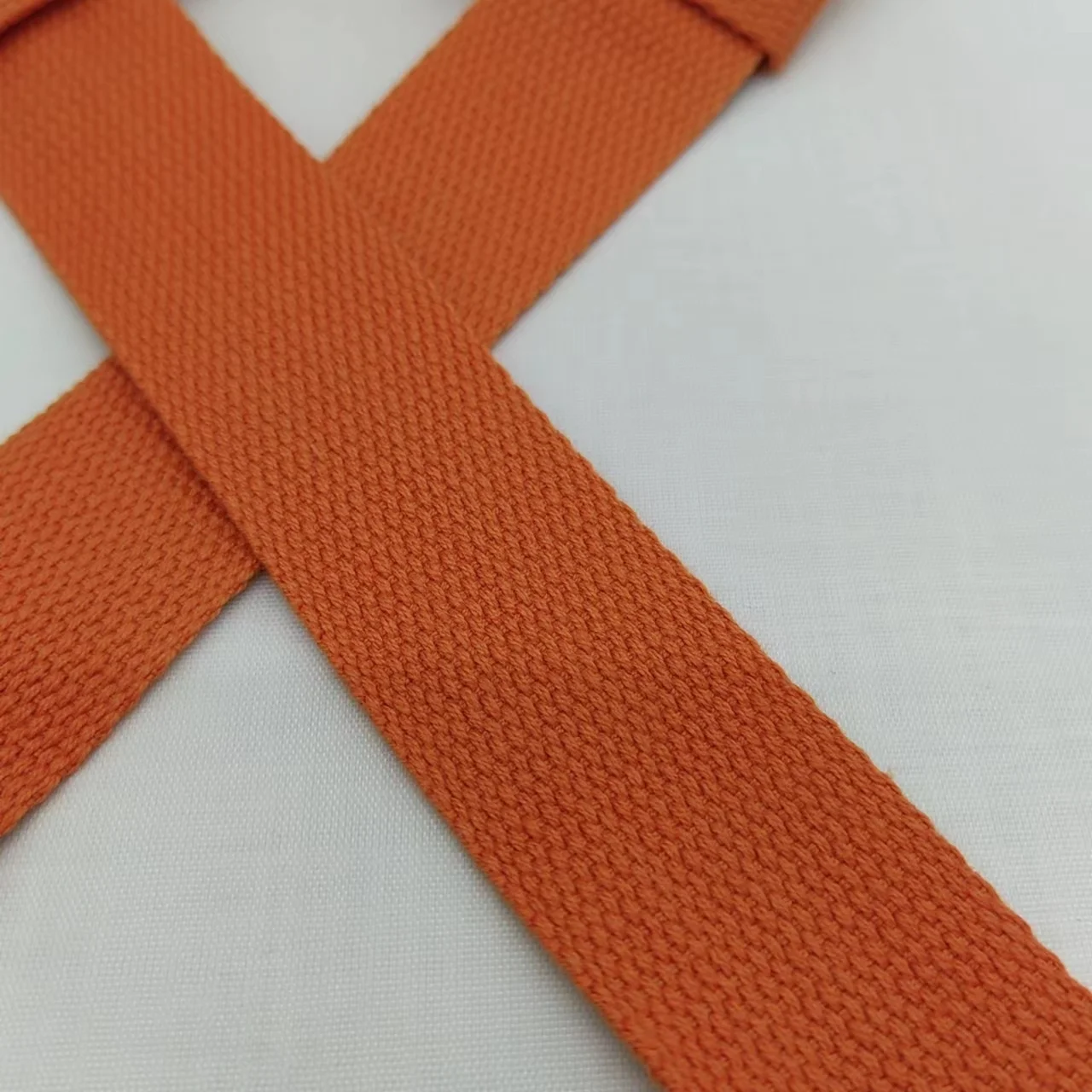 Un primer plano de una prenda de tela de color naranja. Parece ser un cinturón o una correa con textura tejida, posiblemente hecha de un material sintético como poliéster o nailon. El cinturón se coloca plano y se ata con un nudo, que se usa comúnmente para asegurar los extremos juntos.