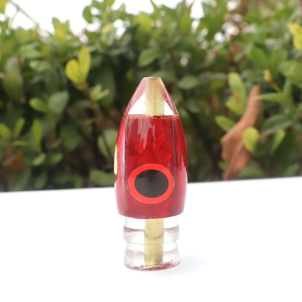 Un elegante objeto en forma de cohete rojo con un acento dorado y un círculo negro, ubicado contra un exuberante fondo verde