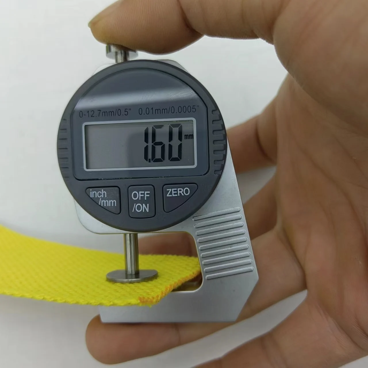 Se utiliza un calibrador digital para medir el espesor de un material amarillo. El calibrador muestra una medida de 160 milímetros, lo que probablemente sea un error o una mala lectura, ya que el calibrador no se está utilizando correctamente para medir el espesor.