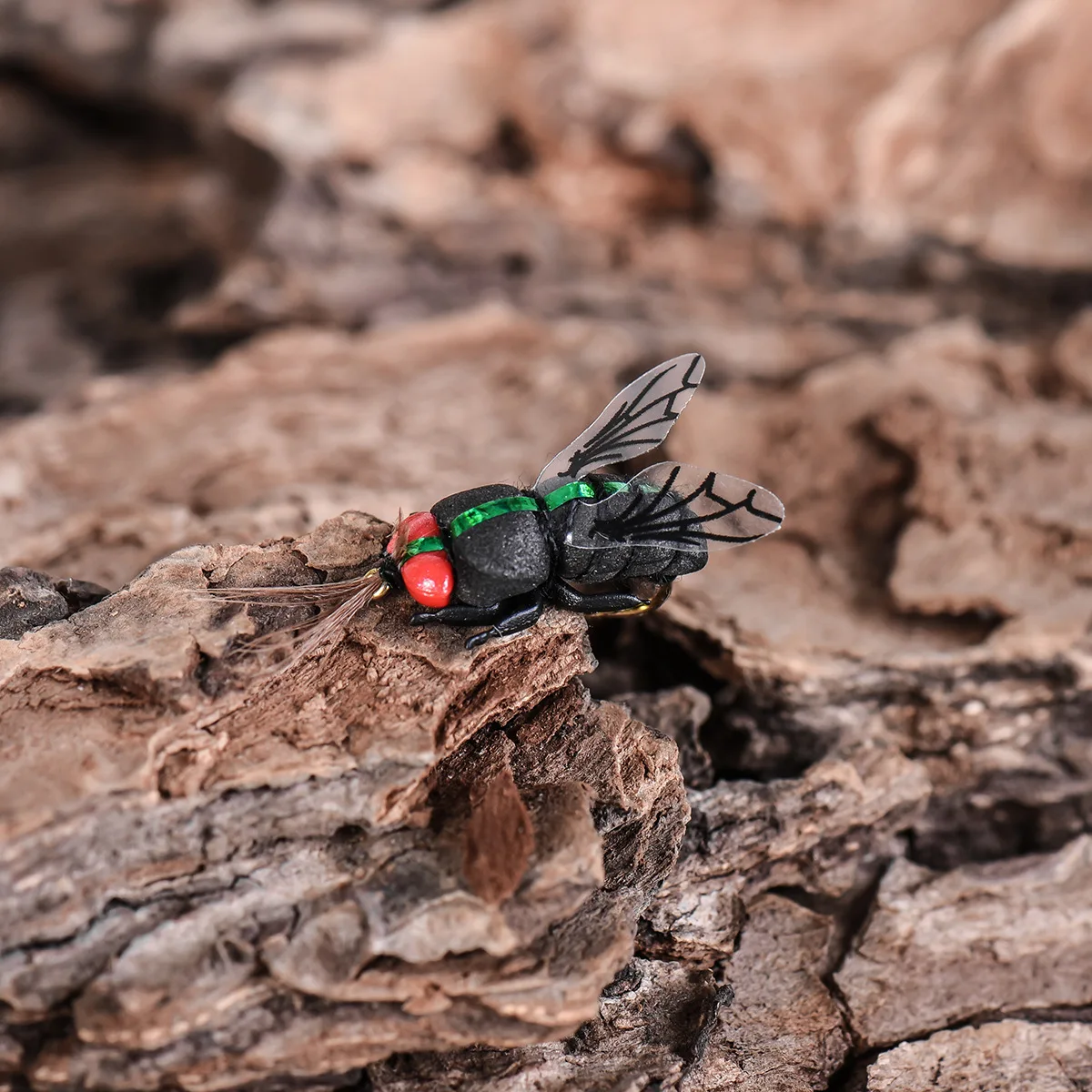 Una mosca negra en miniatura con ojos rojos y acentos verdes descansa sobre corteza texturizada