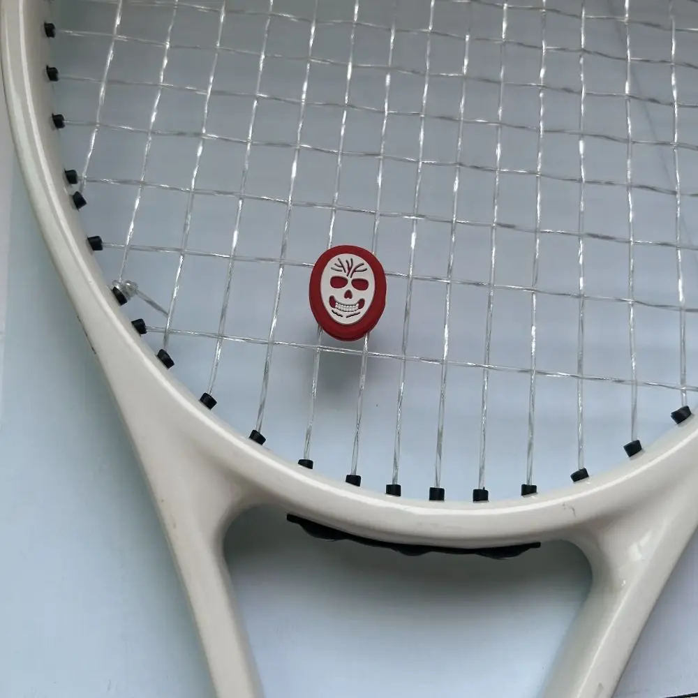 Una raqueta de tenis blanca con un encanto de cara decorativa roja en las cuerdas