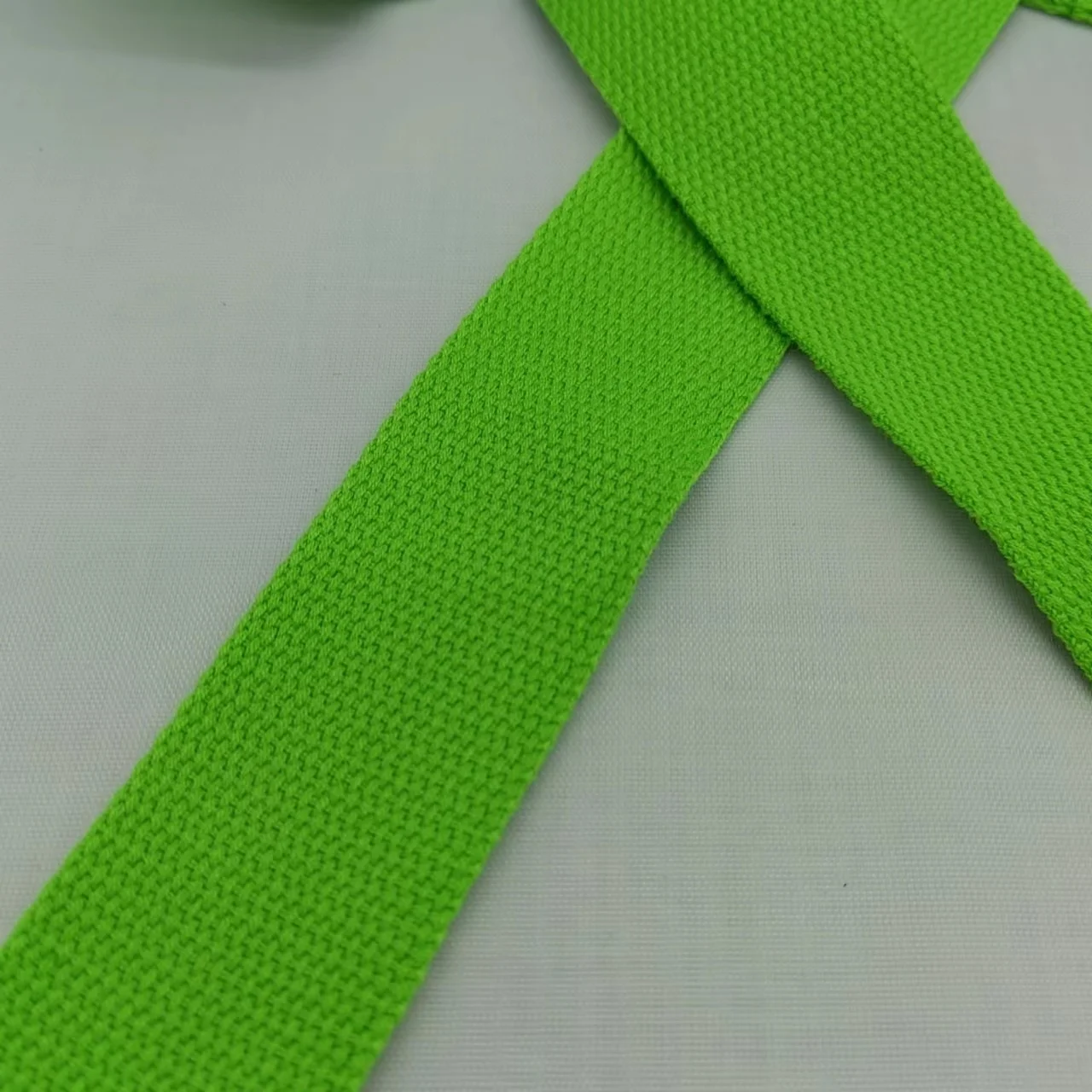 Una prenda de tela verde con textura acanalada, posiblemente un cinturón o una correa. Parece estar extendido sobre una superficie blanca. La tela tiene un patrón de punto o tejido y el color es un verde brillante y sólido.