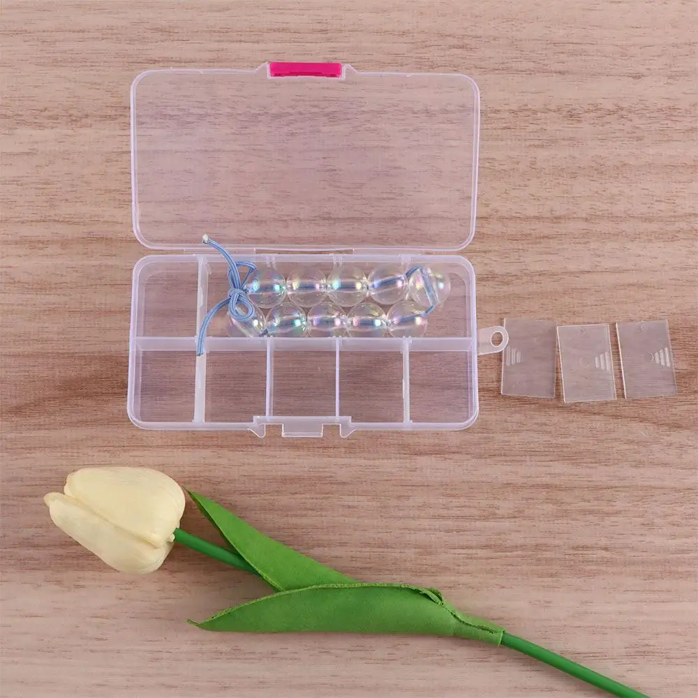 Un recipiente de plástico transparente con compartimentos que contienen una cadena de cuentas iridiscentes, acompañadas de un delicado tulipán amarillo