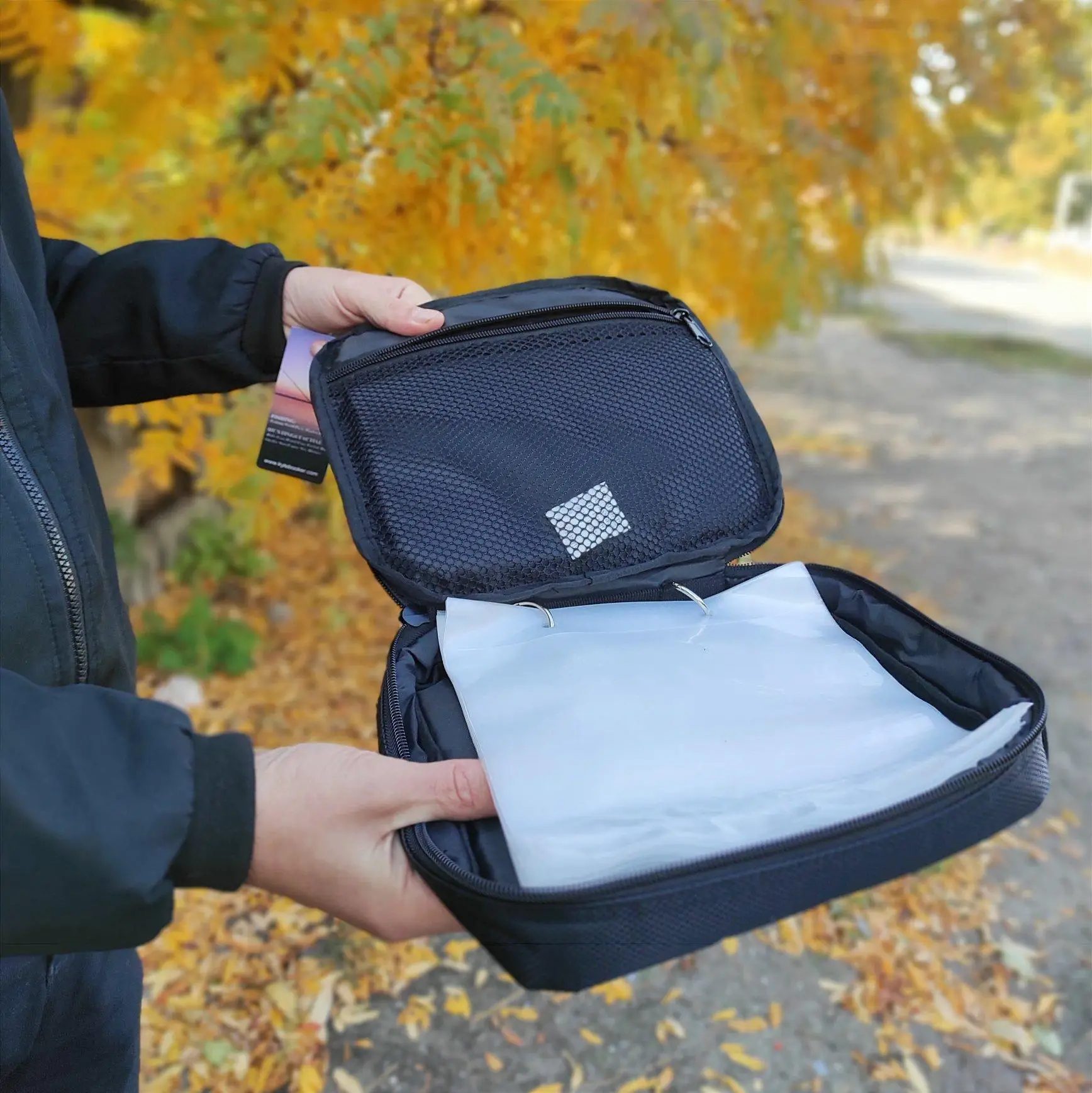 Una persona que sostiene una bolsa abierta o una bolsa pequeña. Dentro de la bolsa, parece haber un trozo de papel doblado o un documento pequeño, que es blanco y tiene un pliegue en el medio, lo que sugiere que ha sido doblado.