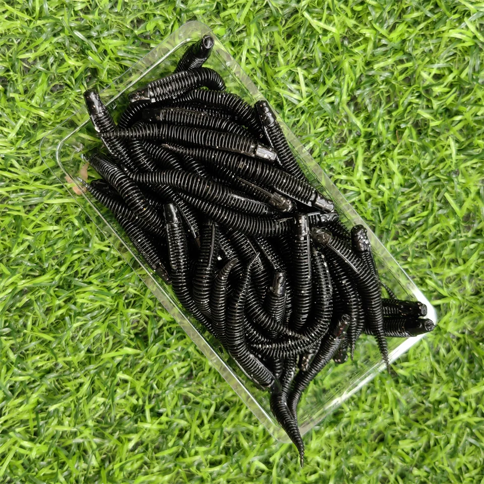 Intrincados gusanos negros que se muestran en una bandeja transparente establecida contra un exuberante fondo verde