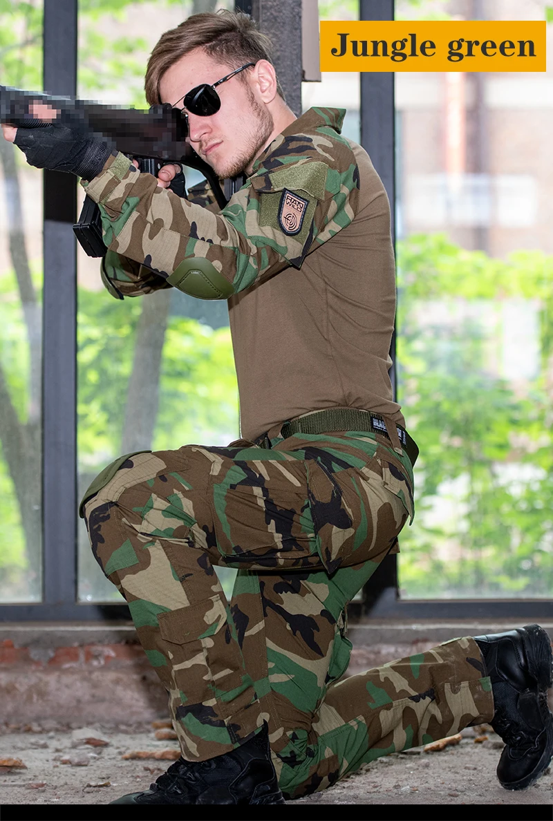 Una persona que viste un uniforme de camuflaje, que parece ser un traje de estilo militar, posiblemente para un ejercicio de simulación o entrenamiento. La persona está arrodillada y apunta con un rifle equipado con una mira telescópica. El fondo sugiere un entorno urbano con una ventana y algo de vegetación visible.