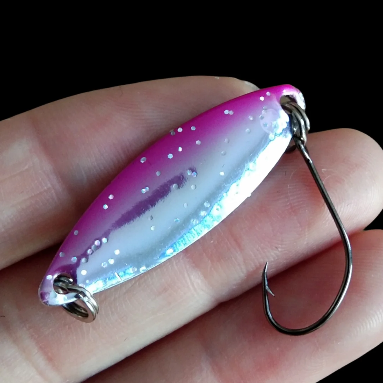Una persona que sostiene un gancho de pesca con un señuelo rosa y plateado