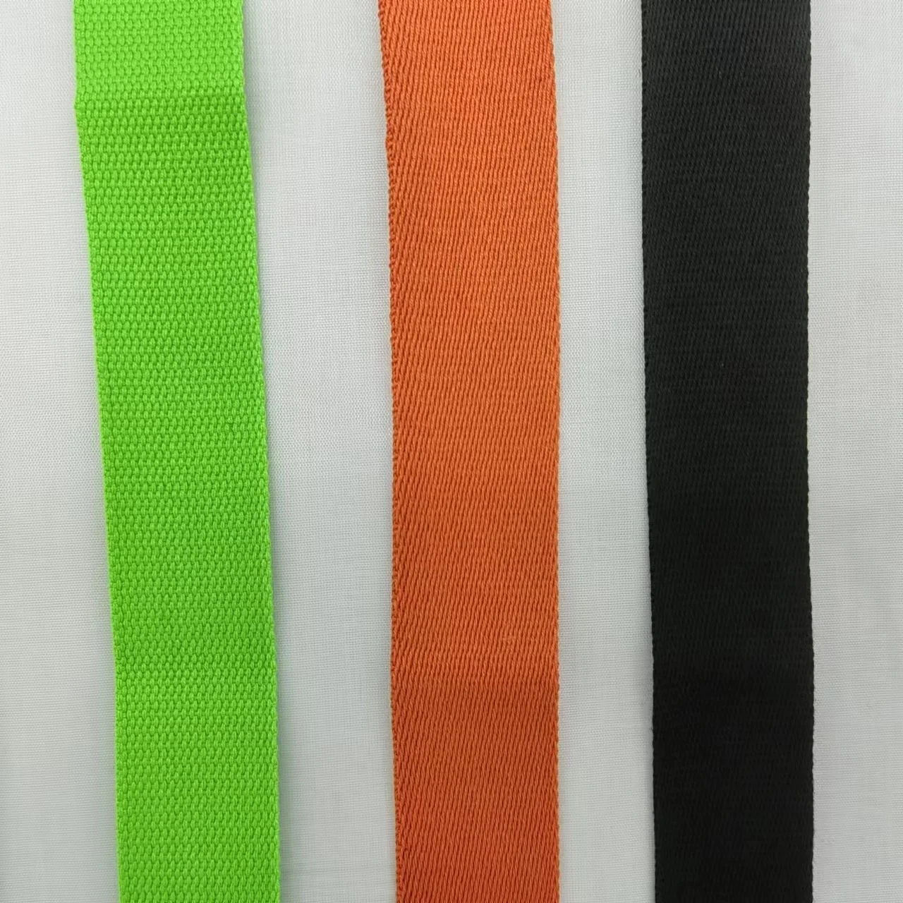 Tres tiras de tela dispuestas una al lado de la otra. De izquierda a derecha, hay una tira de tela verde, una tira de tela blanca y una tira de tela negra. Las franjas verdes y negras parecen tener un tejido texturizado, mientras que la franja blanca parece más suave.
