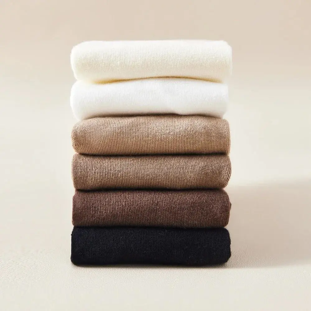 Una pila de seis calcetines cuidadosamente plegados en diferentes tonos de blanco beige y negro