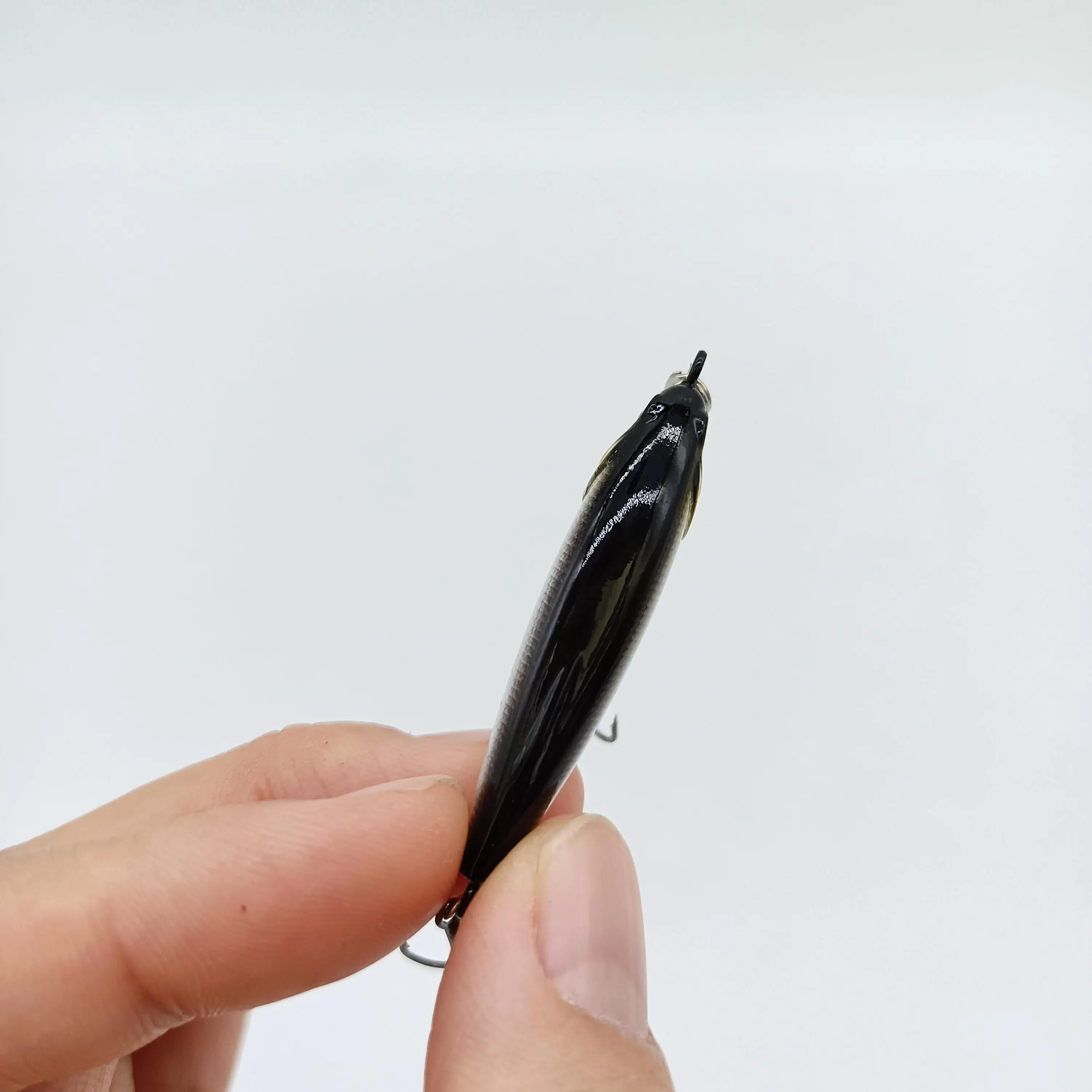 Un elegante señuelo de pesca negra se sostiene delicadamente entre los dedos