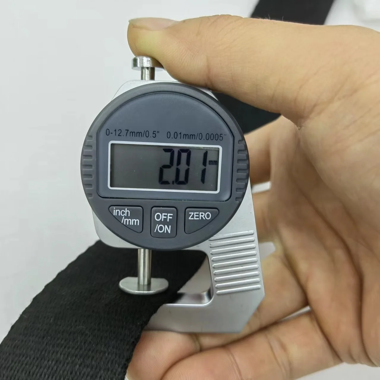 Un calibrador digital sostenido por una persona. El calibrador es una herramienta de medición que se utiliza para medir la distancia entre dos lados opuestos de un objeto. Tiene una pantalla digital que muestra la medida en milímetros y pulgadas, y parece estar midiendo el grosor de una correa o cinturón negro.