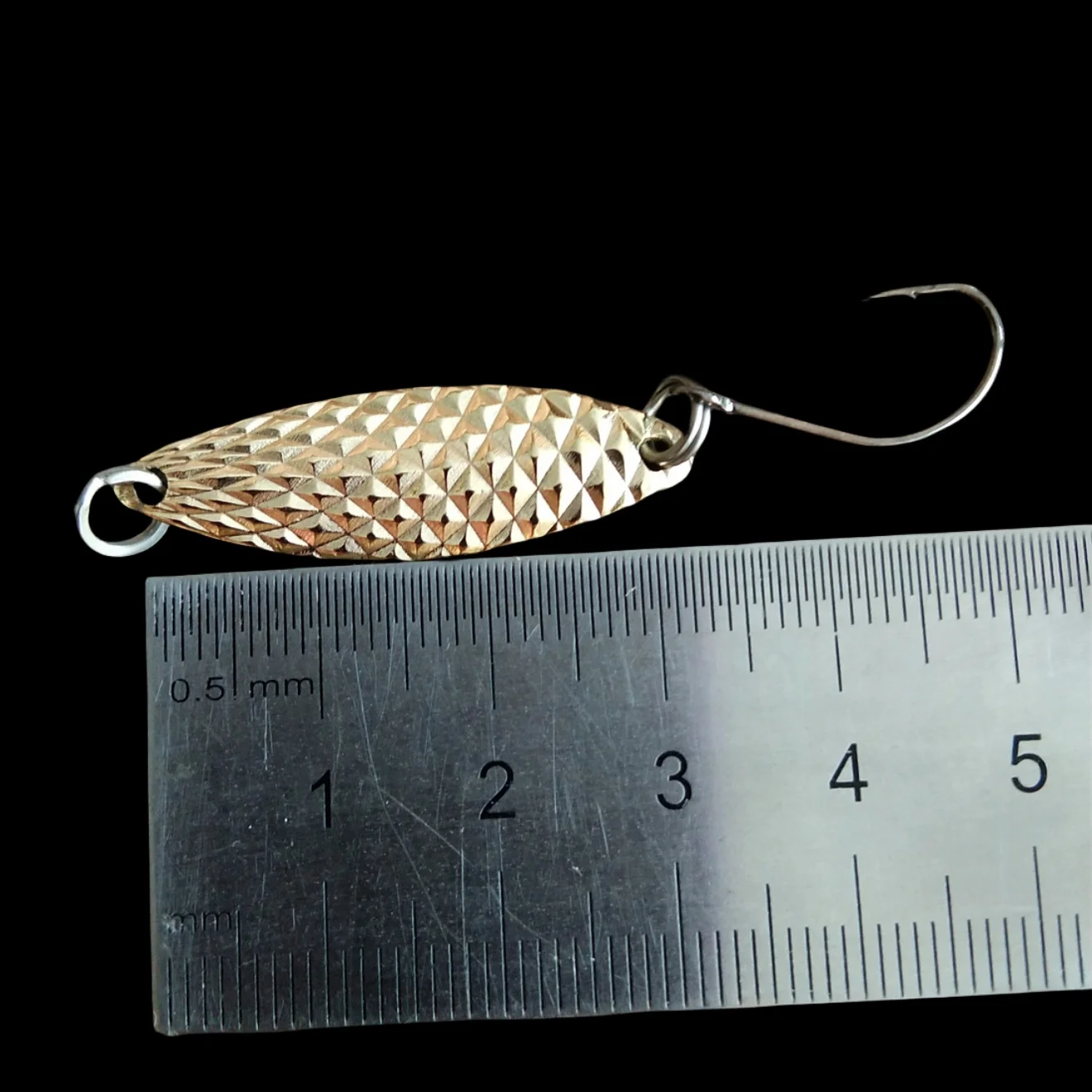 Un gancho con un señuelo de pescado unido está al lado de una regla