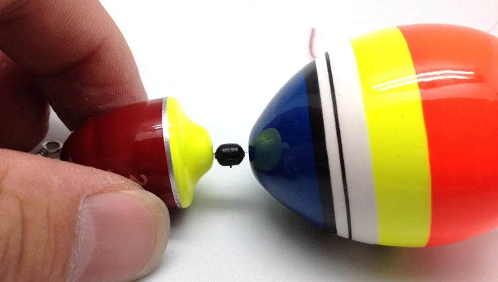 La mano de una persona sosteniendo un objeto rojo y amarillo, que parece ser un juguete o un pequeño elemento decorativo. El objeto tiene un acabado brillante y se sostiene sobre un fondo blanco.