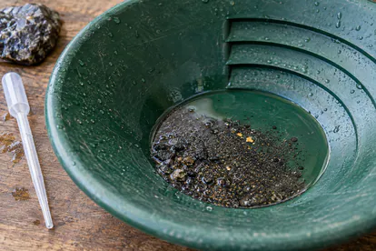 Batea verde con arena negra húmeda y pequeñas partículas doradas sobre una mesa