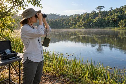 Persona observando una laguna tropical con prismáticos y cuaderno de campo