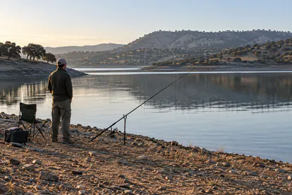 Pescador junto a un embalse de paisaje extremeño preparando una jornada desde la orilla