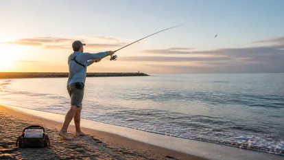Lance de spinning desde una playa con rompiente suave y luz de amanecer.